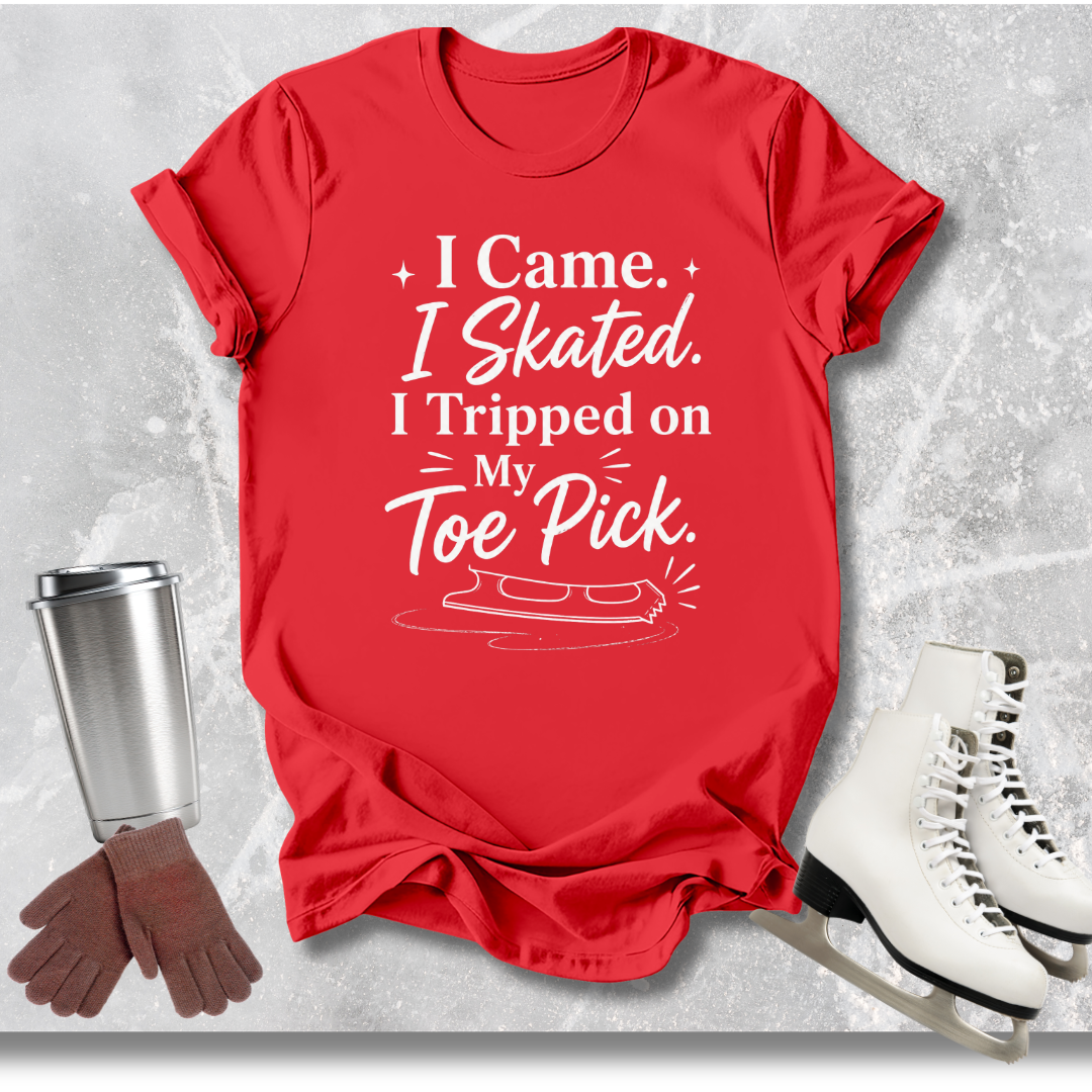 Red t-shirt with humorous ice skating 'I came I skated. I tripped on my toe pick' text, next to ice skates, gloves, and a cup on a textured gray background.