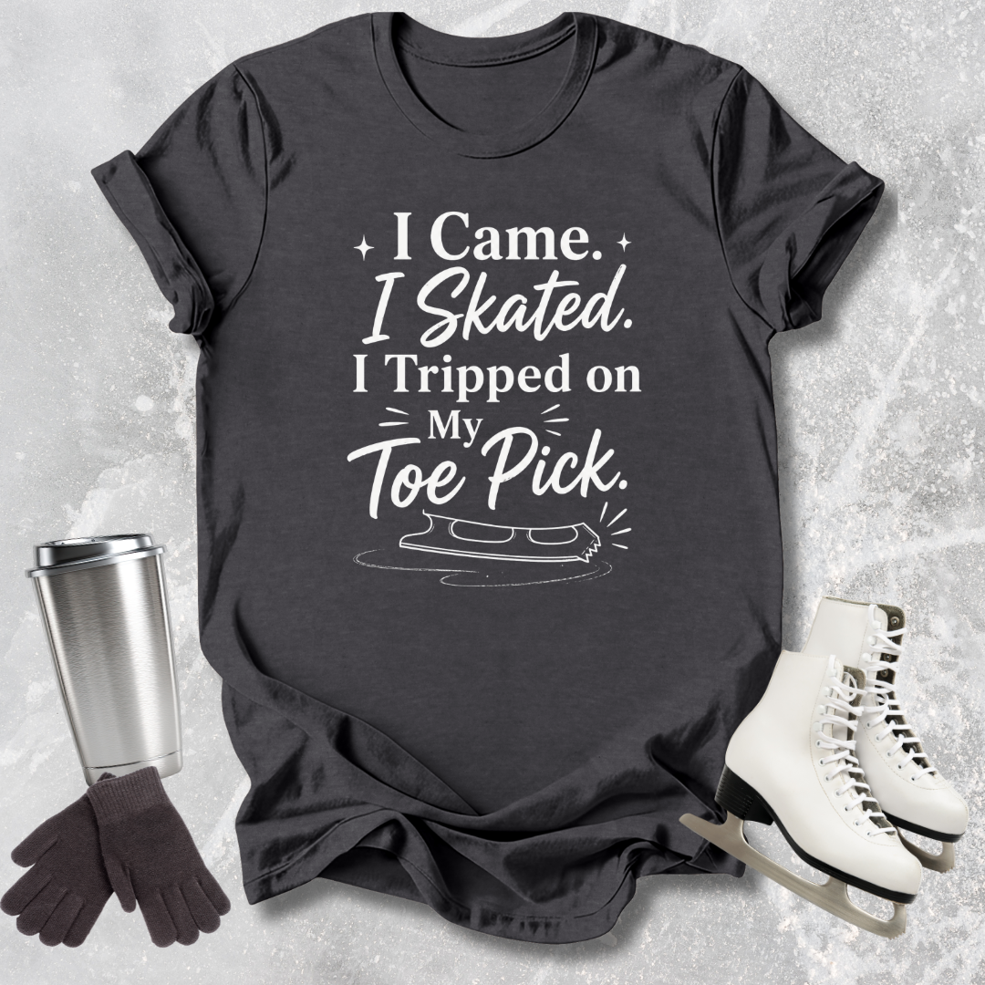Black t-shirt with humorous ice skating 'I came I skated. I tripped on my toe pick' text, next to ice skates and a travel mug on a textured surface.