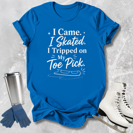 Blue t-shirt with humorous text, next to ice skates, gloves, and a tumbler on a textured gray background.