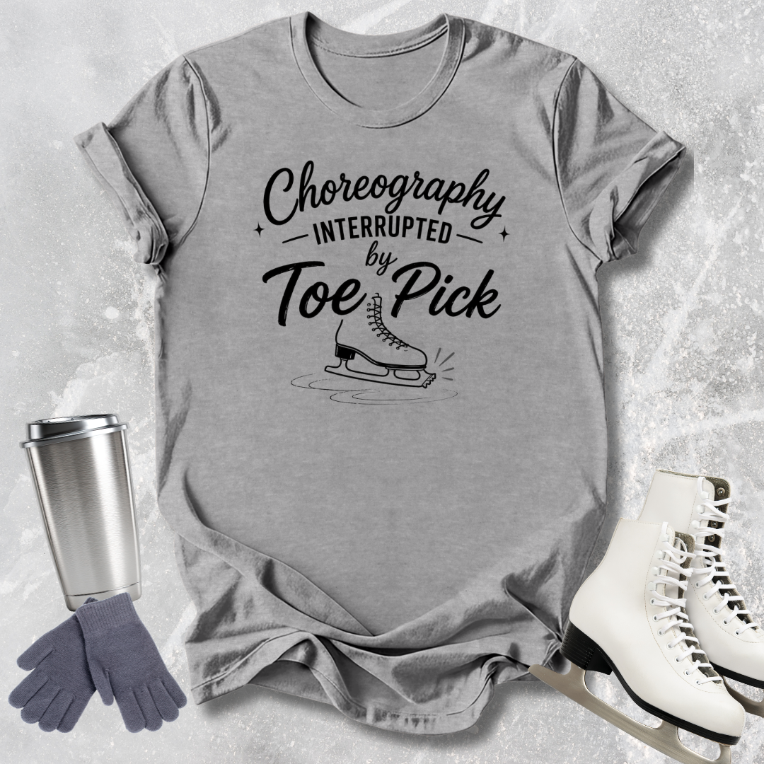 Gray t-shirt with 'Choreography Interrupted by Toe Pick' text and graphic, next to ice skates and a travel mug.