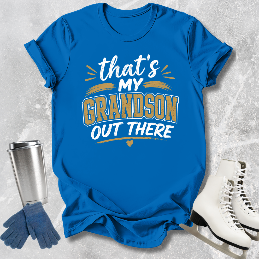 Blue t-shirt with 'That's my grandson out there' text, next to a silver tumbler, blue gloves, and white skates on a textured gray background.
