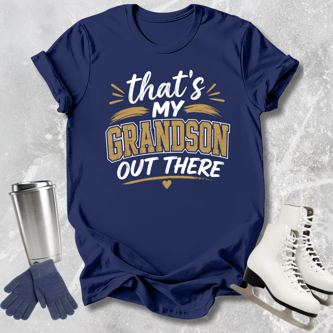 Navy blue t-shirt with 'That's my grandson out there' text, next to a silver tumbler, gloves, and white skates on a textured gray background.