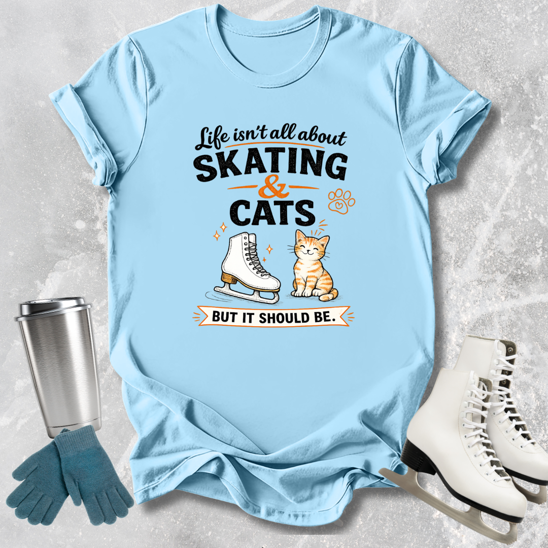 Light blue t-shirt with a humorous design about skating and cats, placed on a textured surface with ice skates and gloves.