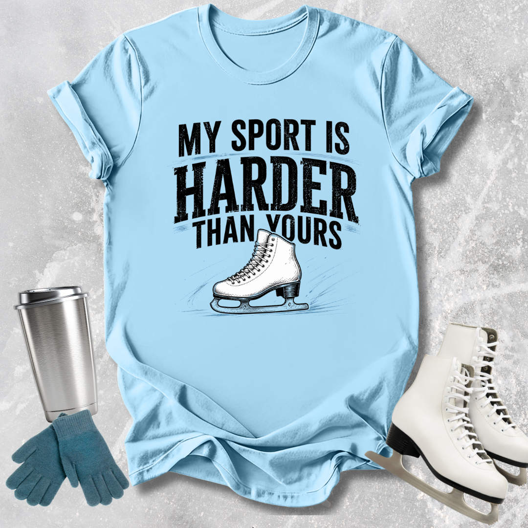 Light blue t-shirt with 'My sport is harder than yours' text and ice skate graphic, surrounded by ice skates and a tumbler.