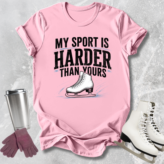 Pink t-shirt with ice skating graphic and text, surrounded by ice skates and a tumbler.