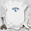 White t-shirt with 'SKATING' print, silver tumbler, gray gloves, and white skates on a textured surface.