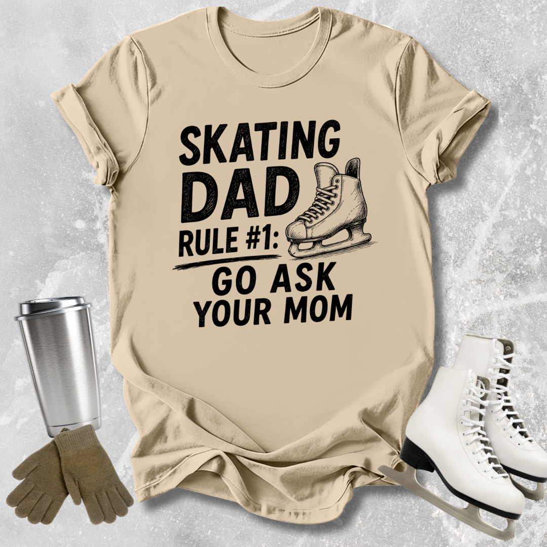 Beige t-shirt with 'Skating Dad' text and graphics on a textured surface with ice skates and gloves.