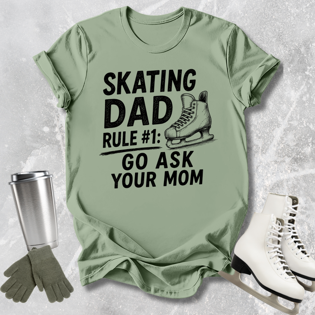 Green t-shirt with 'Skating Dad' text and graphics on a textured surface with ice skates and gloves.