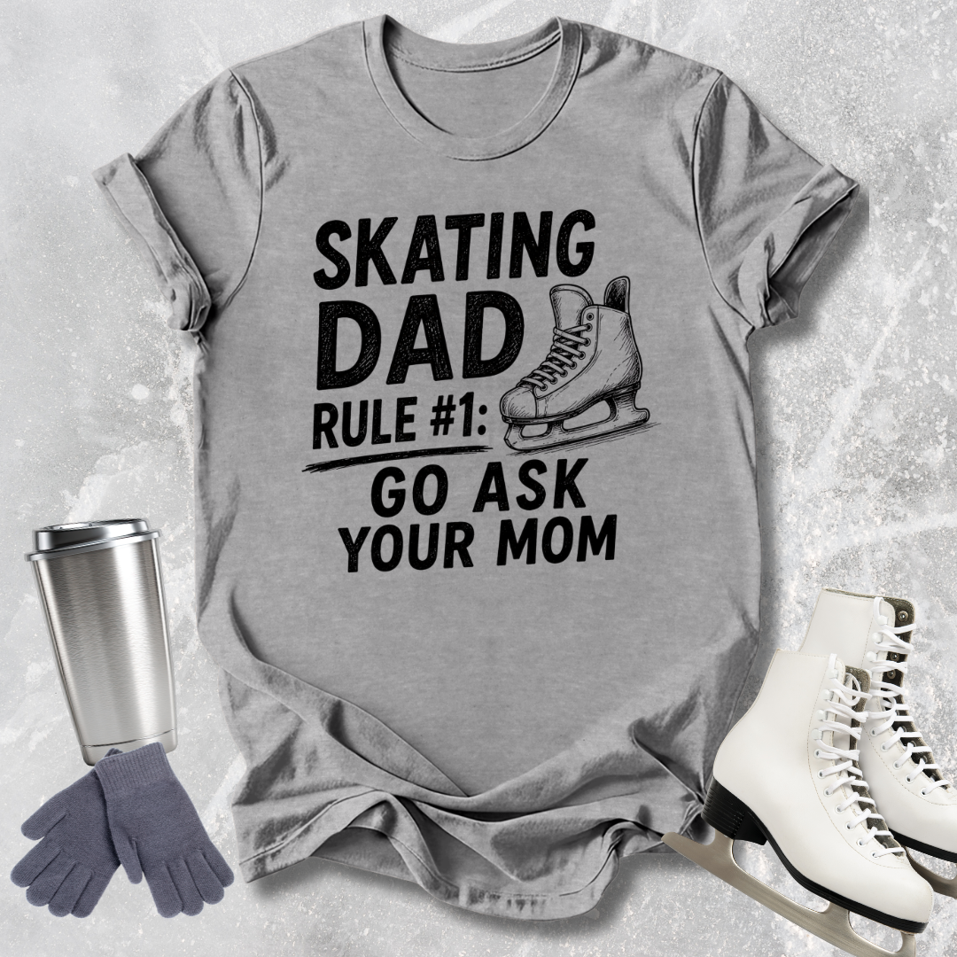 Gray t-shirt with 'Skating Dad' text, ice skates, gloves, and a tumbler on a textured surface.