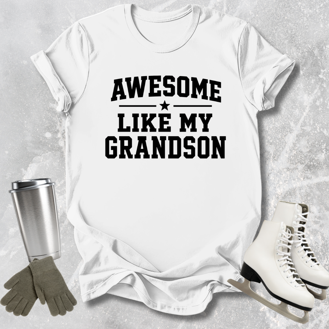 White t-shirt with 'Awesome Like My Grandson' text, surrounded by a tumbler, gloves, and skates on a textured surface.