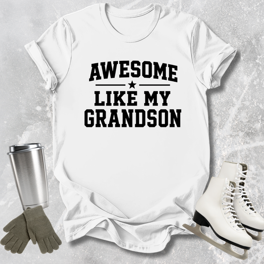 White t-shirt with 'Awesome Like My Grandson' text, surrounded by a tumbler, gloves, and skates on a textured surface.
