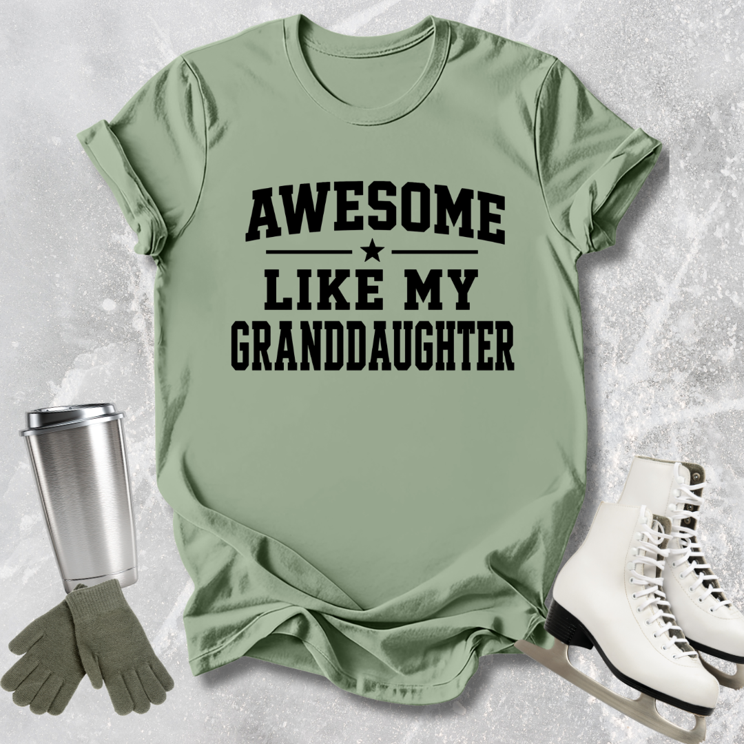 Green t-shirt with 'Awesome like my granddaughter' text, next to a silver tumbler, green gloves, and white skates on a textured surface.