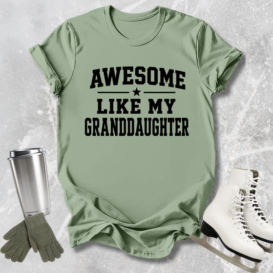 Green t-shirt with 'Awesome like my granddaughter' text, next to a silver tumbler, green gloves, and white skates on a textured surface.