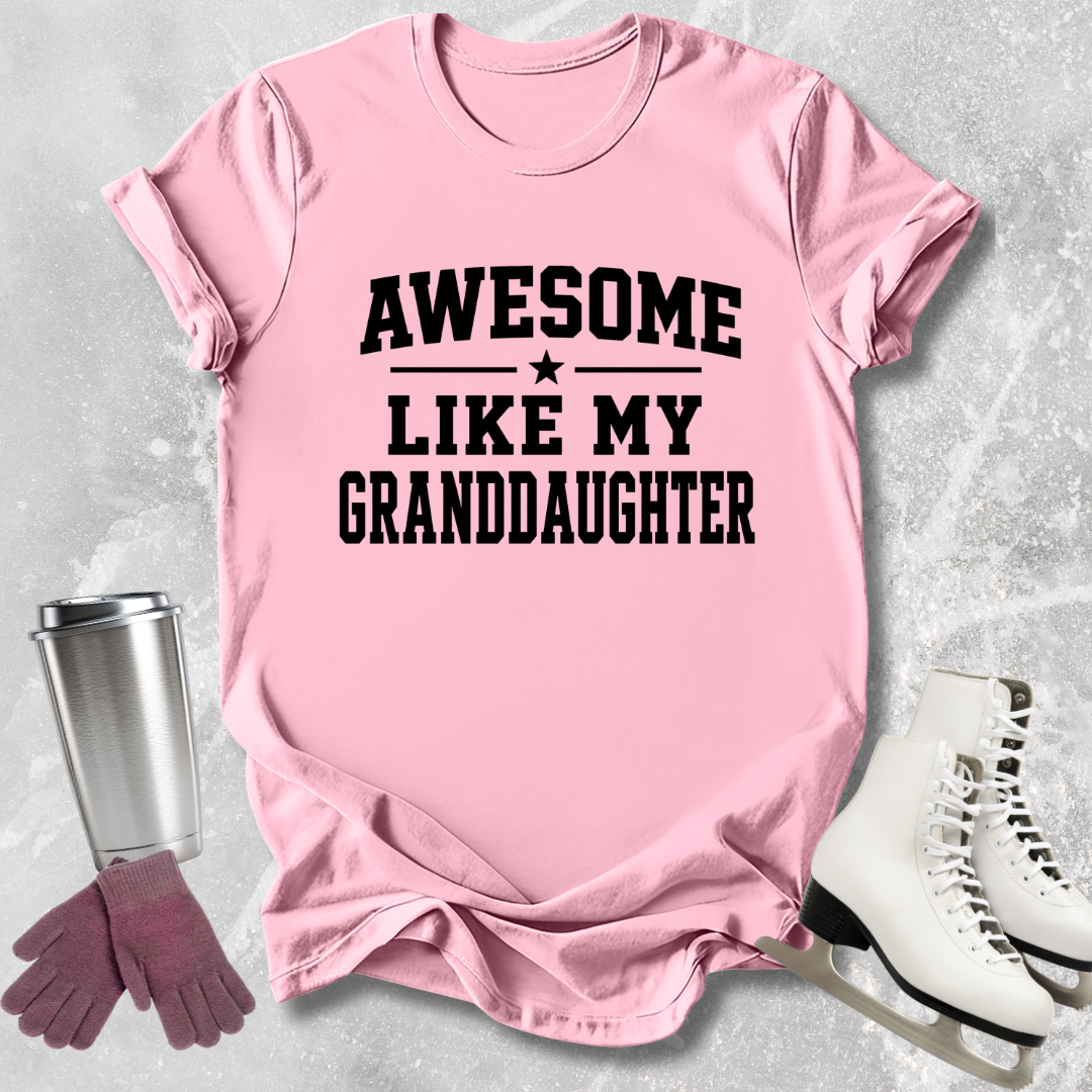 Pink t-shirt with 'Awesome like my granddaughter' text, next to a silver tumbler, pink gloves, and white skates on a light gray background.