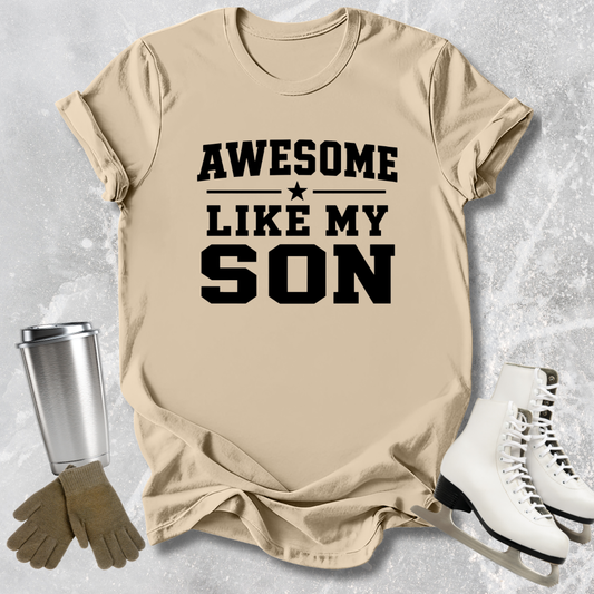 Beige t-shirt with 'Awesome Like My Son' text, next to a silver tumbler, brown gloves, and white skates on a light gray background.
