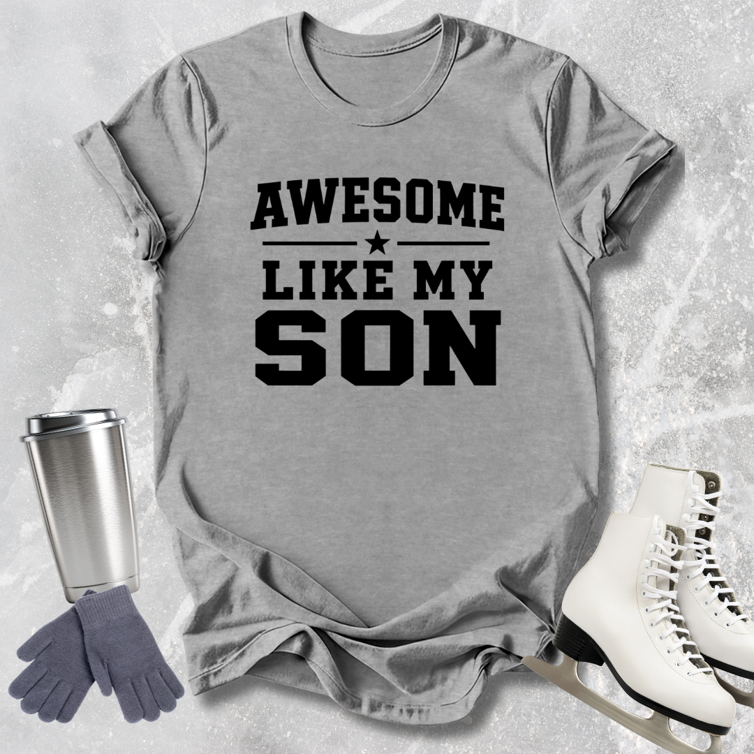 Gray t-shirt with 'Awesome like my son' text, next to a silver tumbler, gray gloves, and white skates on a textured surface.