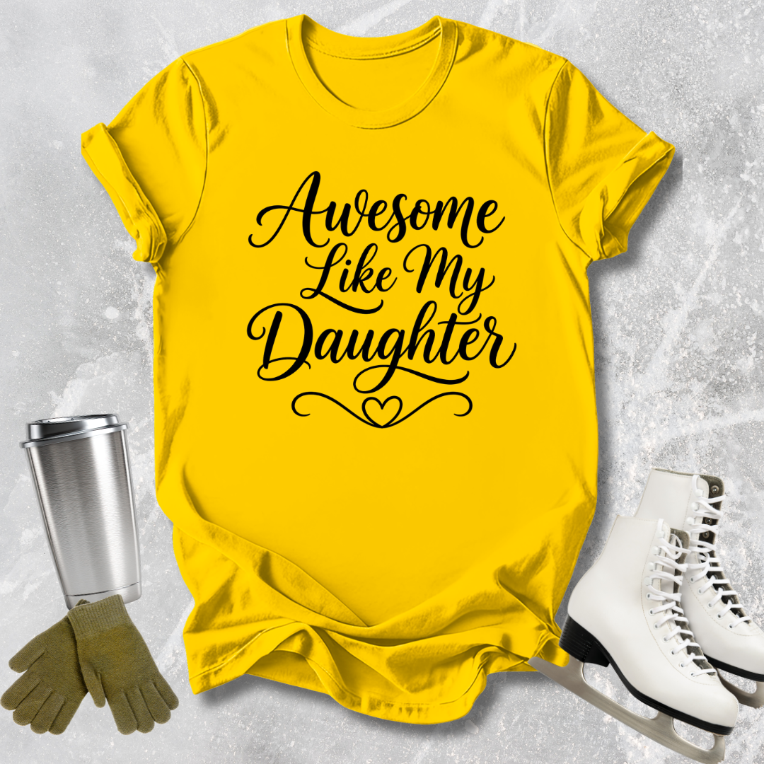 Yellow t-shirt with 'Awesome Like My Daughter' text, next to a silver tumbler, green gloves, and white skates on a textured gray background.
