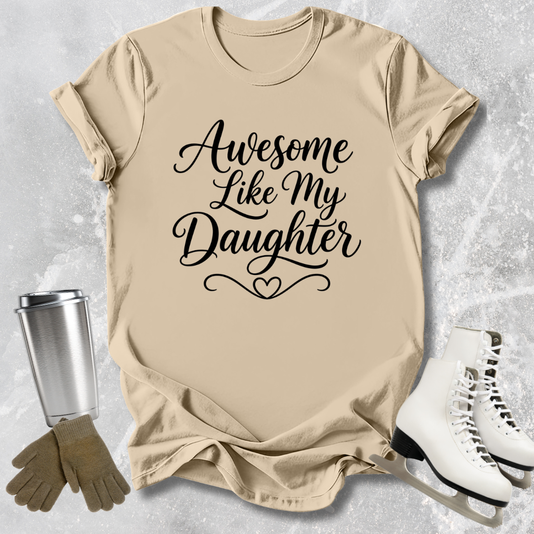 Beige t-shirt with 'Awesome Like My Daughter' text, next to a silver tumbler, brown gloves, and white skates on a light gray background.