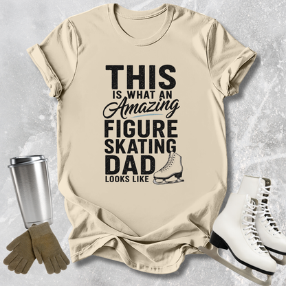 Beige t-shirt with text 'This is what an amazing figure skating dad looks like' on a textured surface with ice skates and gloves.