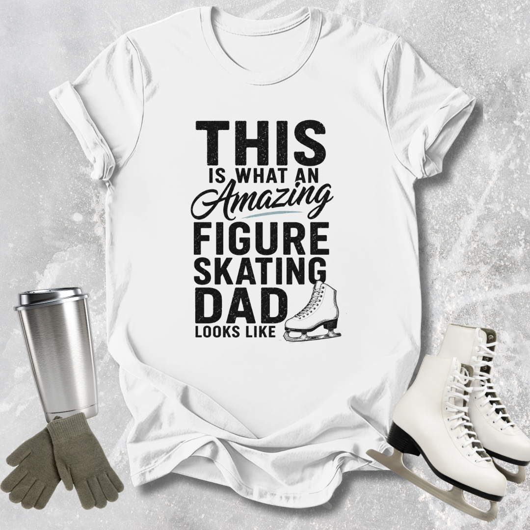White t-shirt with text 'This is what an amazing figure skating dad looks like' on a textured surface with ice skates, gloves, and a tumbler.