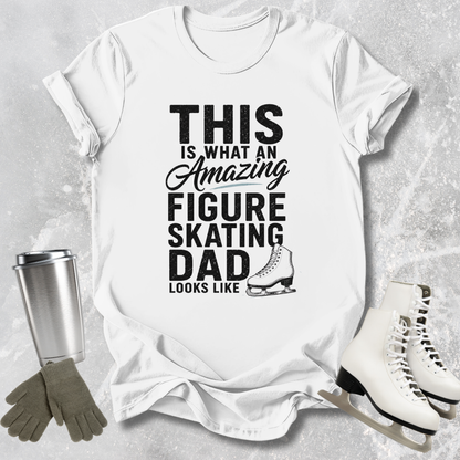 White t-shirt with text 'This is what an amazing figure skating dad looks like' on a textured surface with ice skates, gloves, and a tumbler.