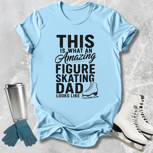 Light blue t-shirt with text 'This is what an amazing figure skating dad looks like' on a textured surface with ice skates and gloves.