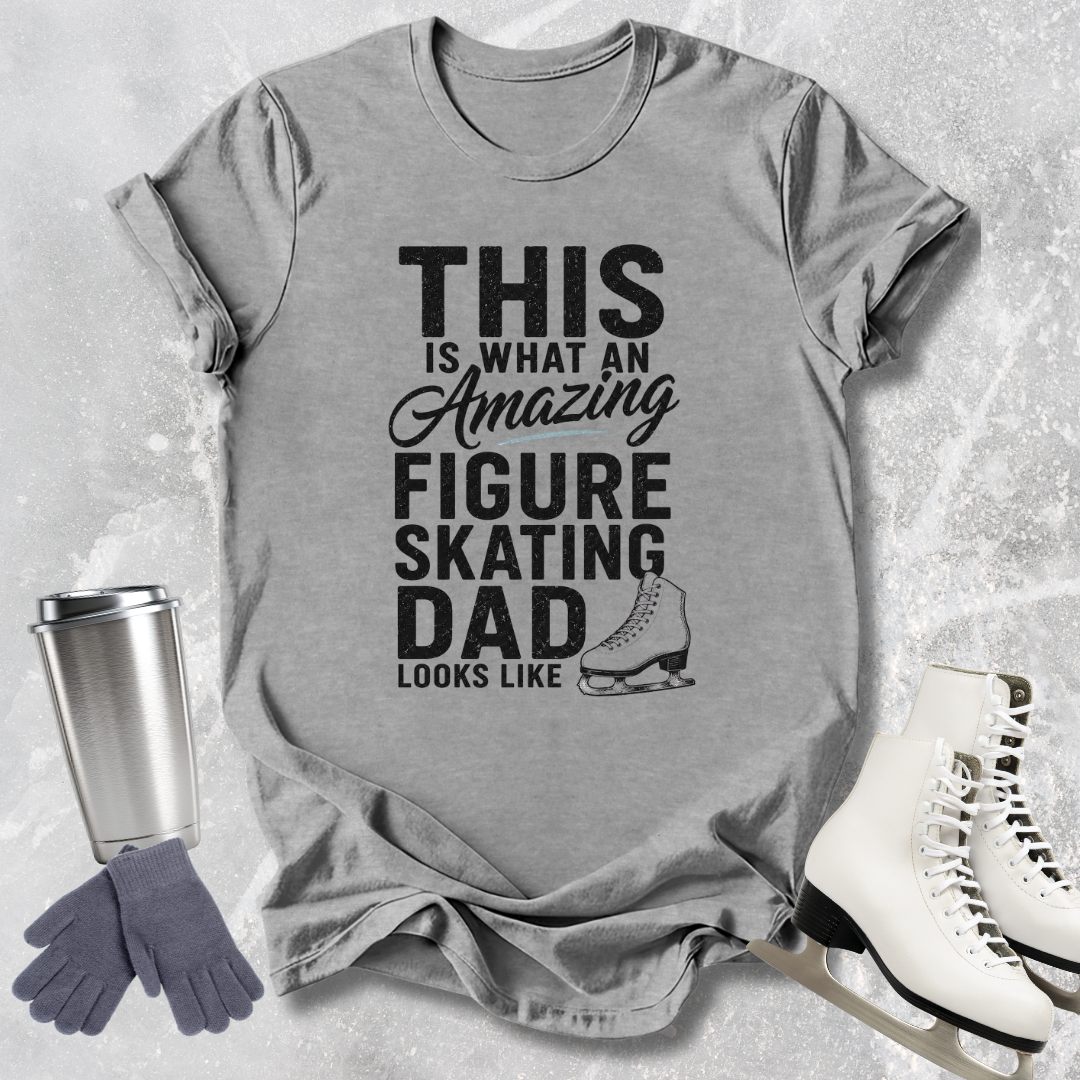 Gray t-shirt with text 'This is what an amazing figure skating dad looks like' on a textured surface with ice skates and a tumbler.