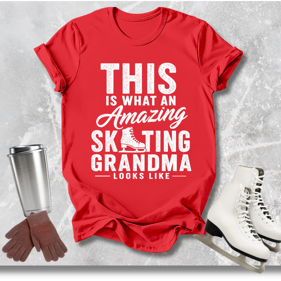 Red t-shirt with text 'This is what an amazing skating grandma looks like' on a textured gray background with ice skates, gloves, and a cup.