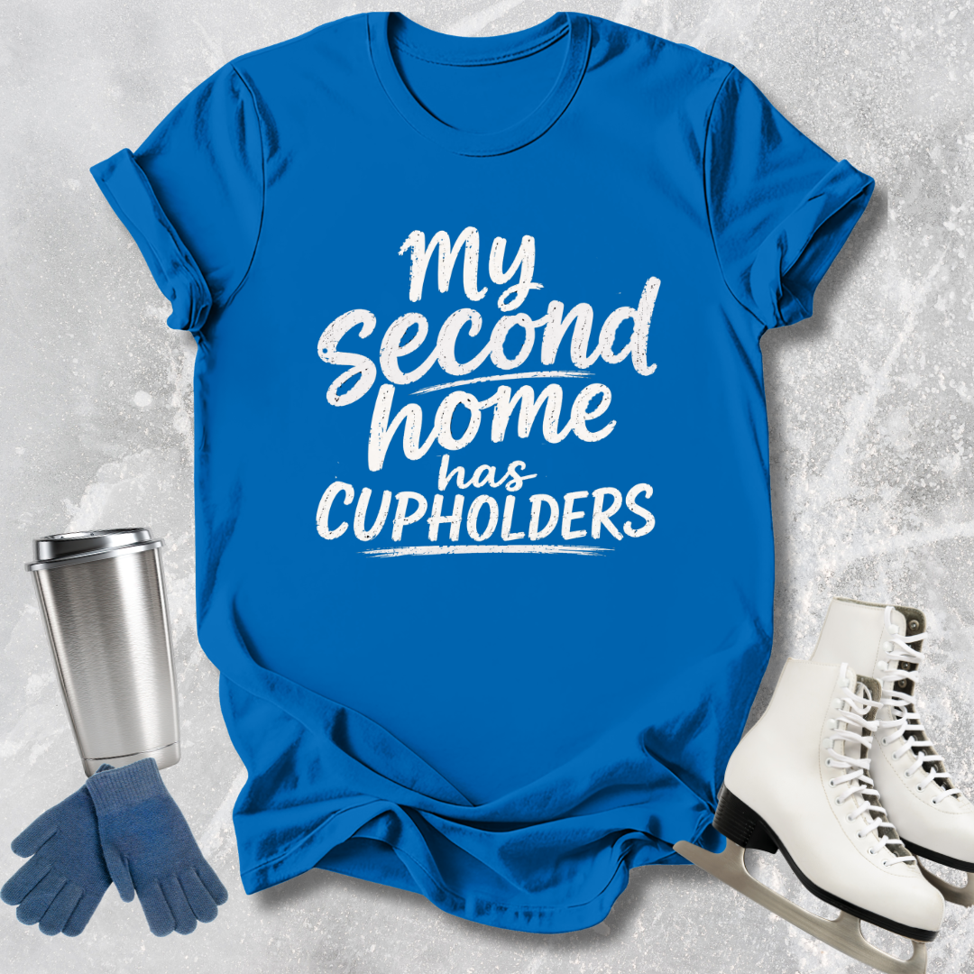 Blue t-shirt with 'My second home has cupholders' text, next to a silver tumbler, blue gloves, and white skates on a textured gray background.