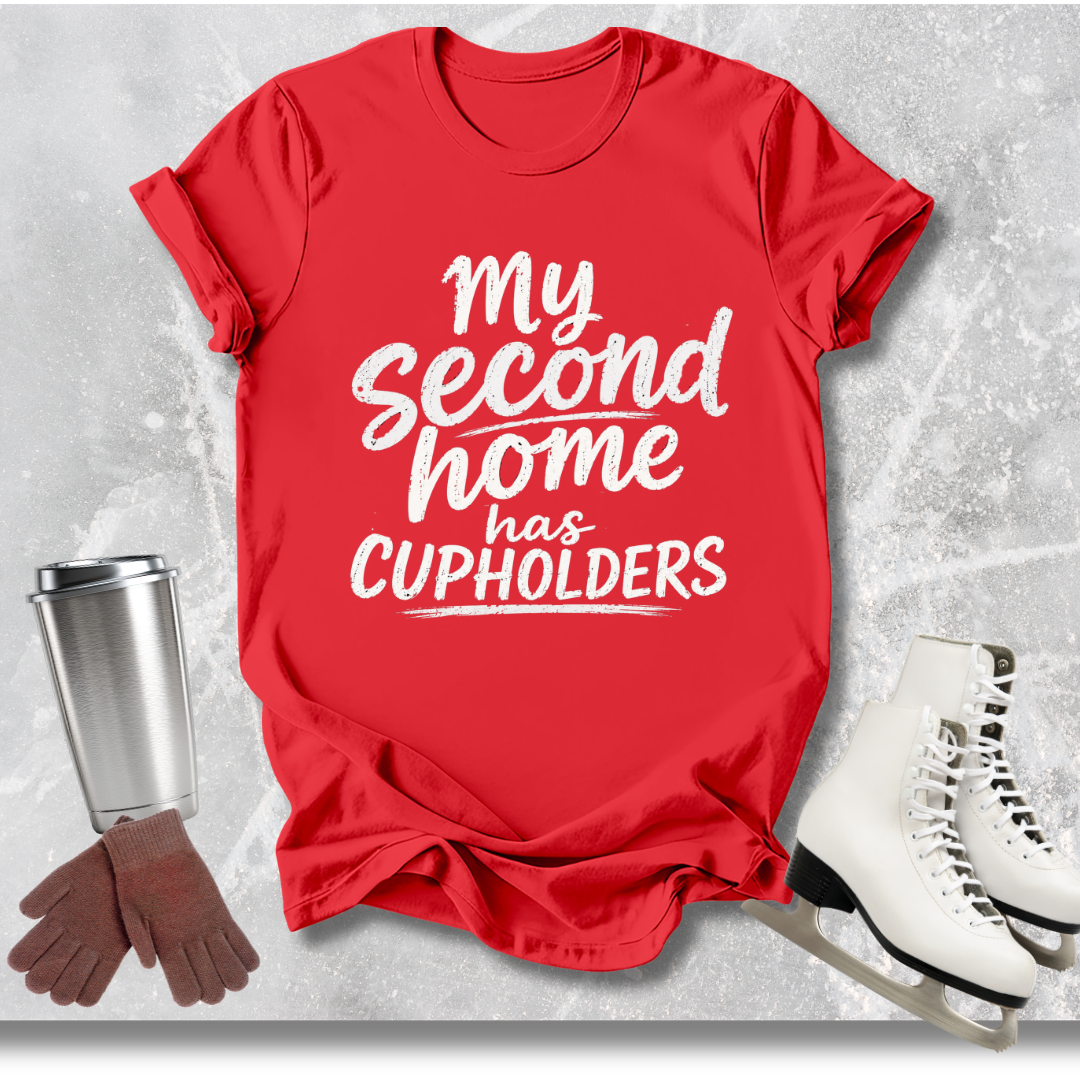 Red t-shirt with 'My second home has cupholders' text, next to a silver tumbler, brown gloves, and white skates on a light gray background.
