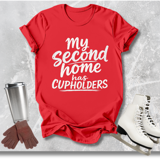 Red t-shirt with 'My second home has cupholders' text, next to a silver tumbler, brown gloves, and white skates on a light gray background.