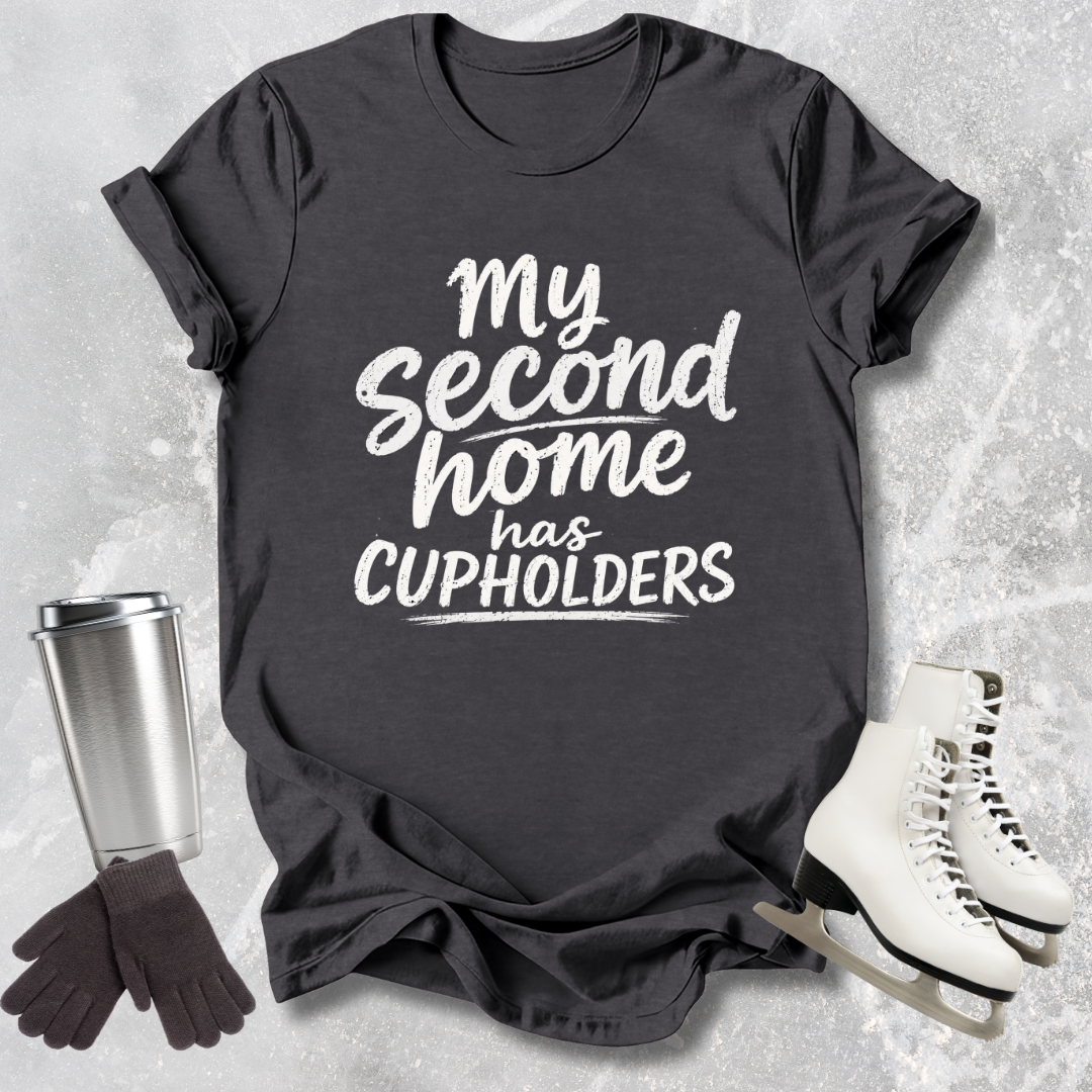 Black t-shirt with 'My second home has cupholders' text, next to a silver tumbler, black gloves, and white skates on a textured surface.