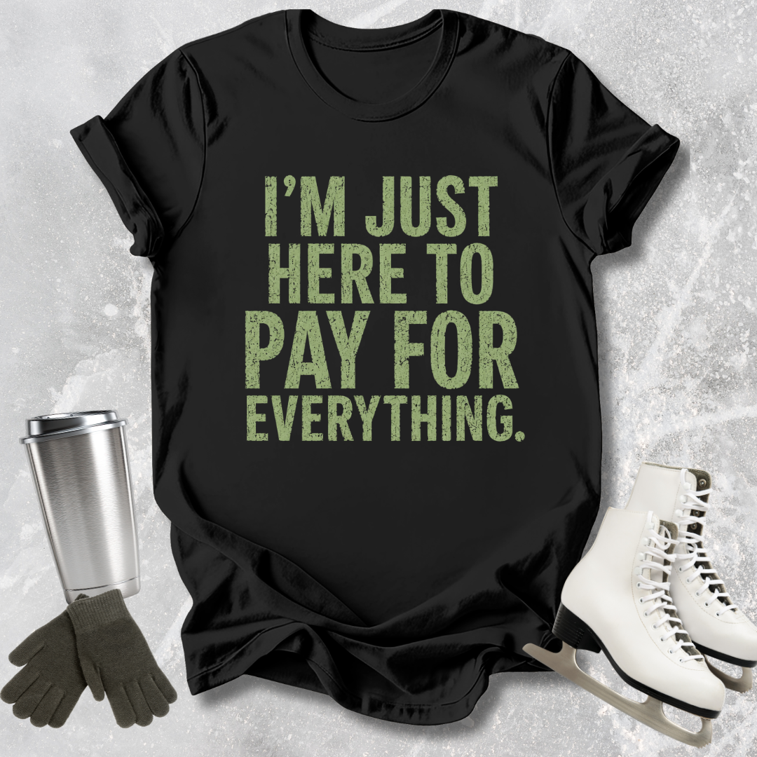 Black t-shirt with green text 'I'm just here to pay for everything' on a textured surface with accessories.