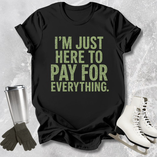 Black t-shirt with green text 'I'm just here to pay for everything' on a textured surface with accessories.