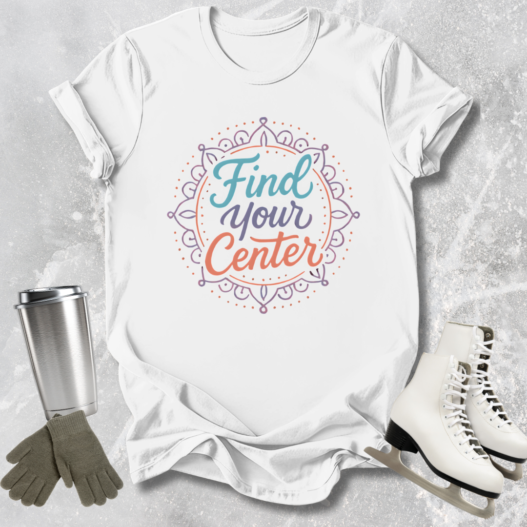 White t-shirt with 'Find Your Center' design, surrounded by a tumbler, gloves, and ice skates on a textured surface.