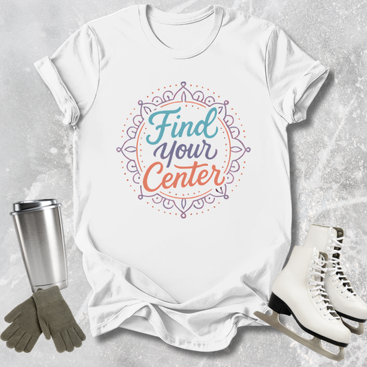 White t-shirt with 'Find Your Center' design, surrounded by a tumbler, gloves, and ice skates on a textured surface.