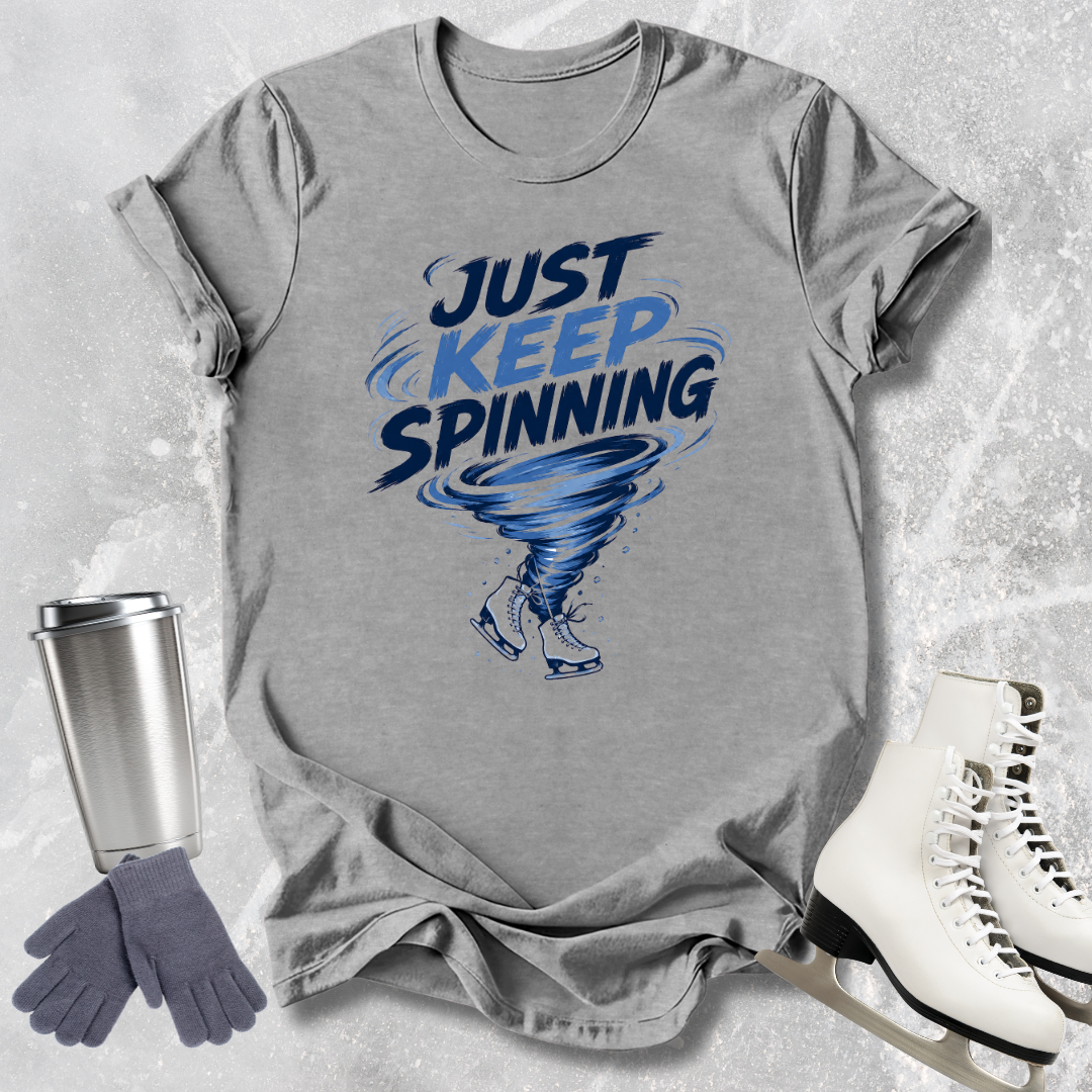 Gray t-shirt with 'Just Keep Spinning' graphic on a textured surface with accessories.