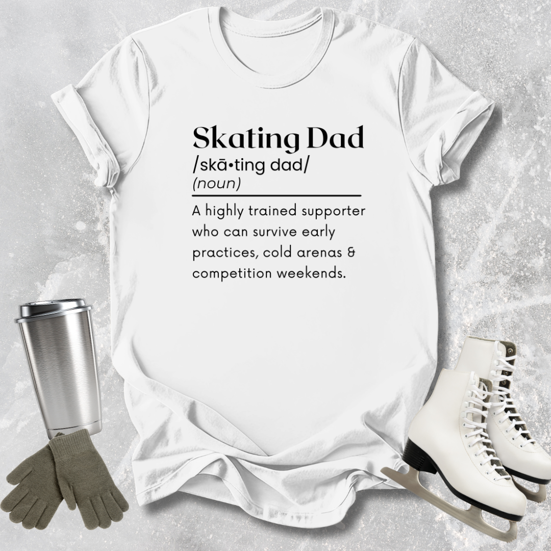 White t-shirt with 'Skating Dad' definition text, surrounded by ice skates, gloves, and a tumbler on a textured surface.