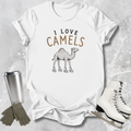 White t-shirt with 'I Love Camels' graphic, surrounded by a tumbler, gloves, and ice skates on a textured surface.