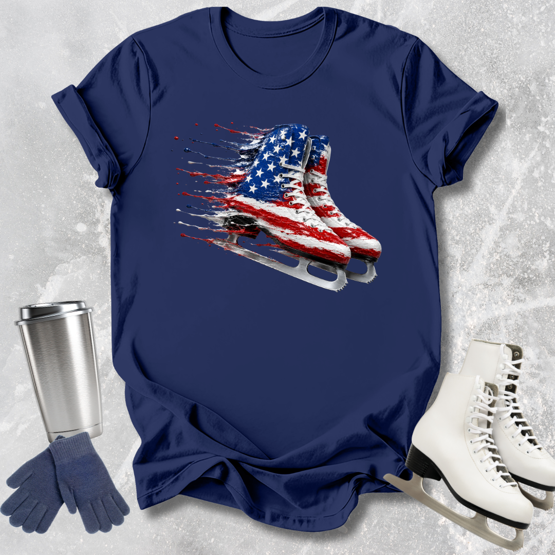 Navy blue t-shirt with American flag ice skate design, next to a silver tumbler, gloves, and white ice skates on a textured gray background.