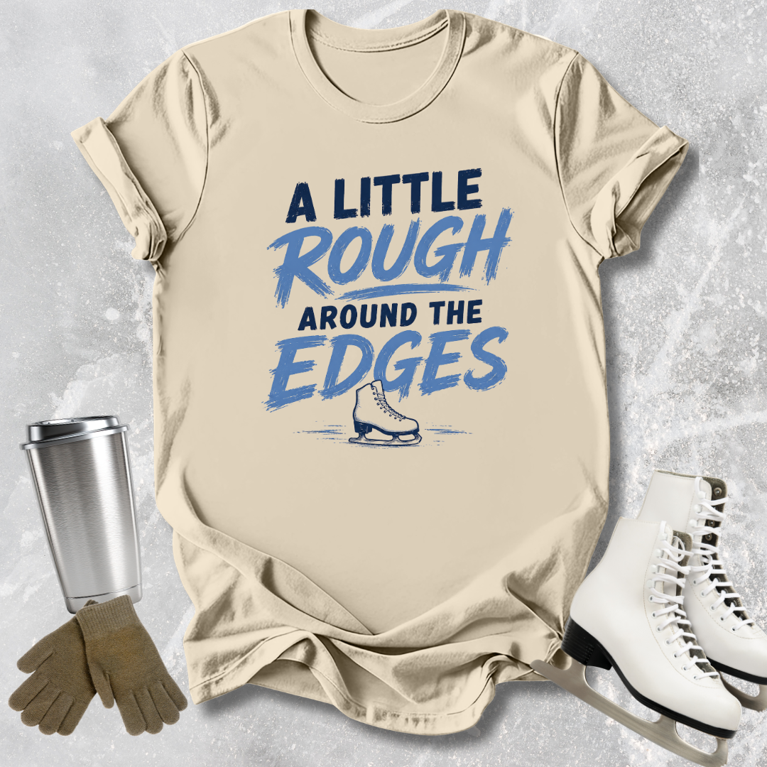 Beige t-shirt with 'A Little Rough Around The Edges' text and graphic, next to ice skates and a tumbler.