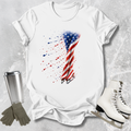 White t-shirt with American flag design, next to a silver tumbler, gray gloves, and white skates on a textured surface.