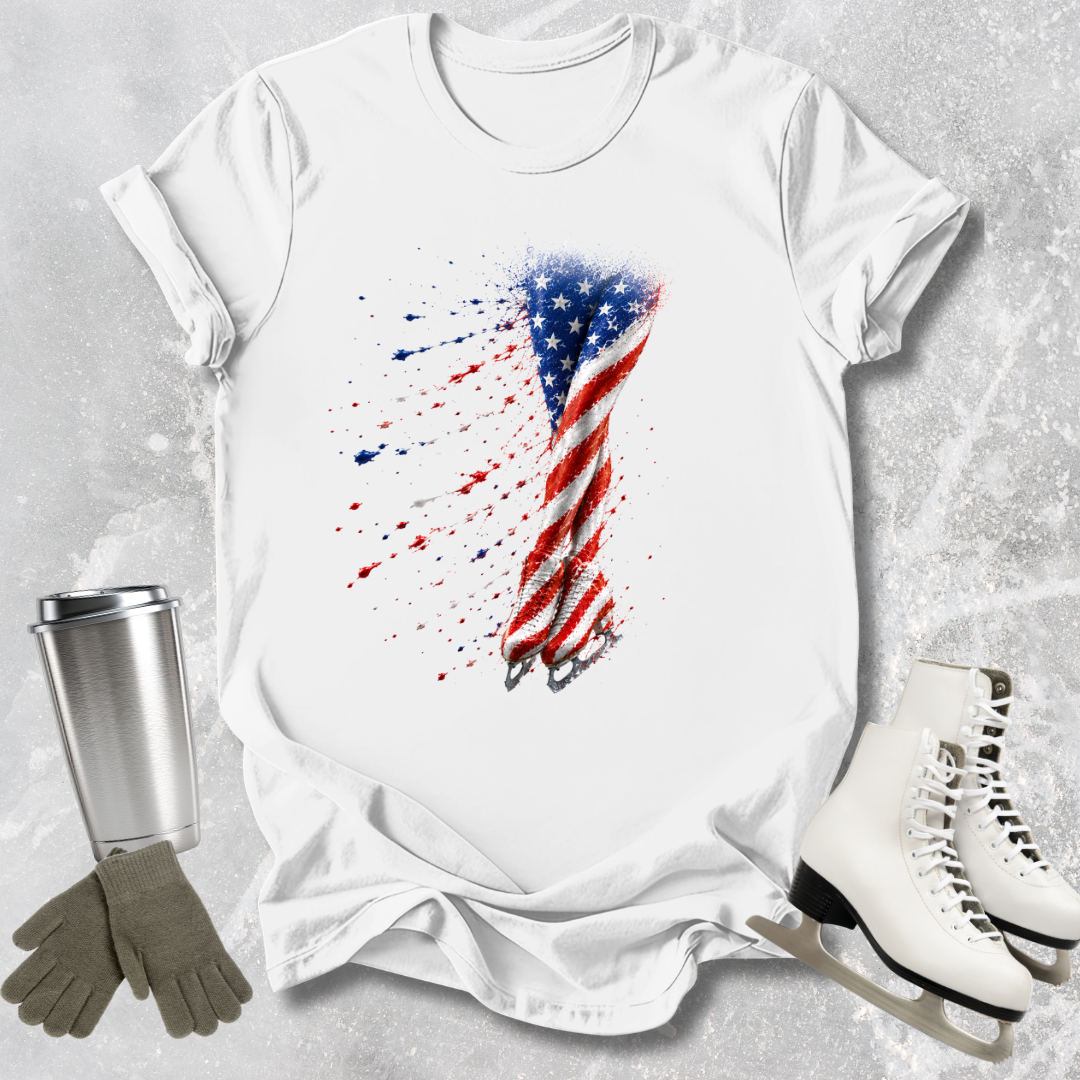 White t-shirt with American flag design, next to a silver tumbler, gray gloves, and white skates on a textured surface.