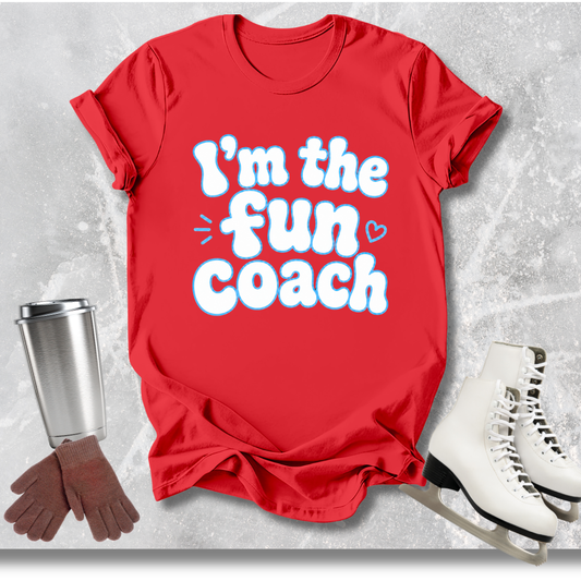 Red t-shirt with 'I'm the fun coach' text, next to a silver tumbler, brown gloves, and white skates on a light gray background.
