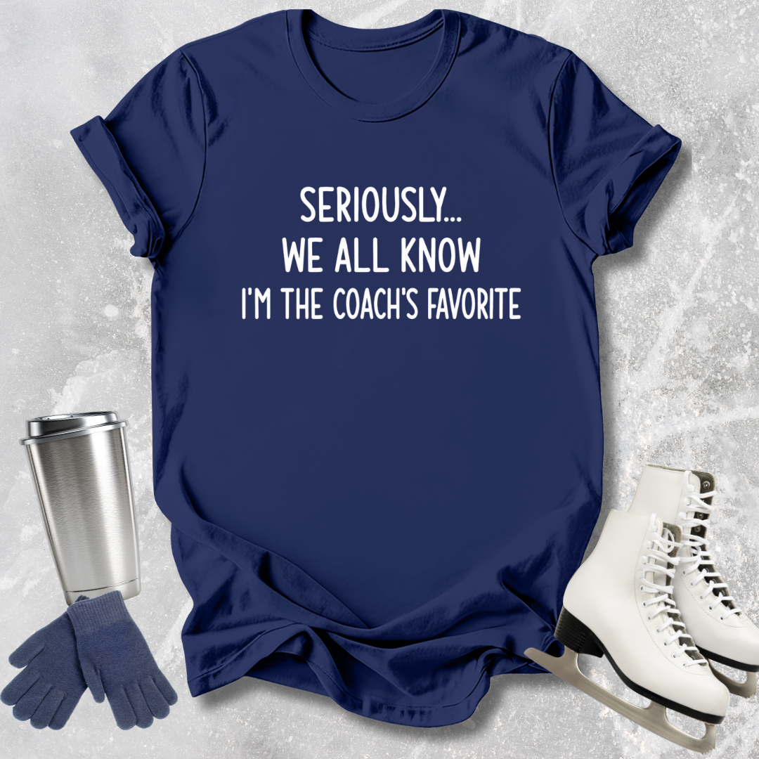 Navy blue t-shirt with text 'Seriously... We all know I'm the coach's favorite' on a textured surface with accessories.