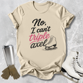 Beige  t-shirt with 'No, I can't triple Axel' text, ice skates, gloves, and a tumbler on a textured surface.