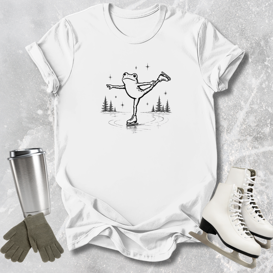 White t-shirt with a graphic of a frog on ice skates, surrounded by ice skates, gloves, and a tumbler on a textured surface.