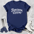 Navy blue t-shirt with 'Figure Skating Legend' text, next to ice skates and a tumbler on a textured gray background.