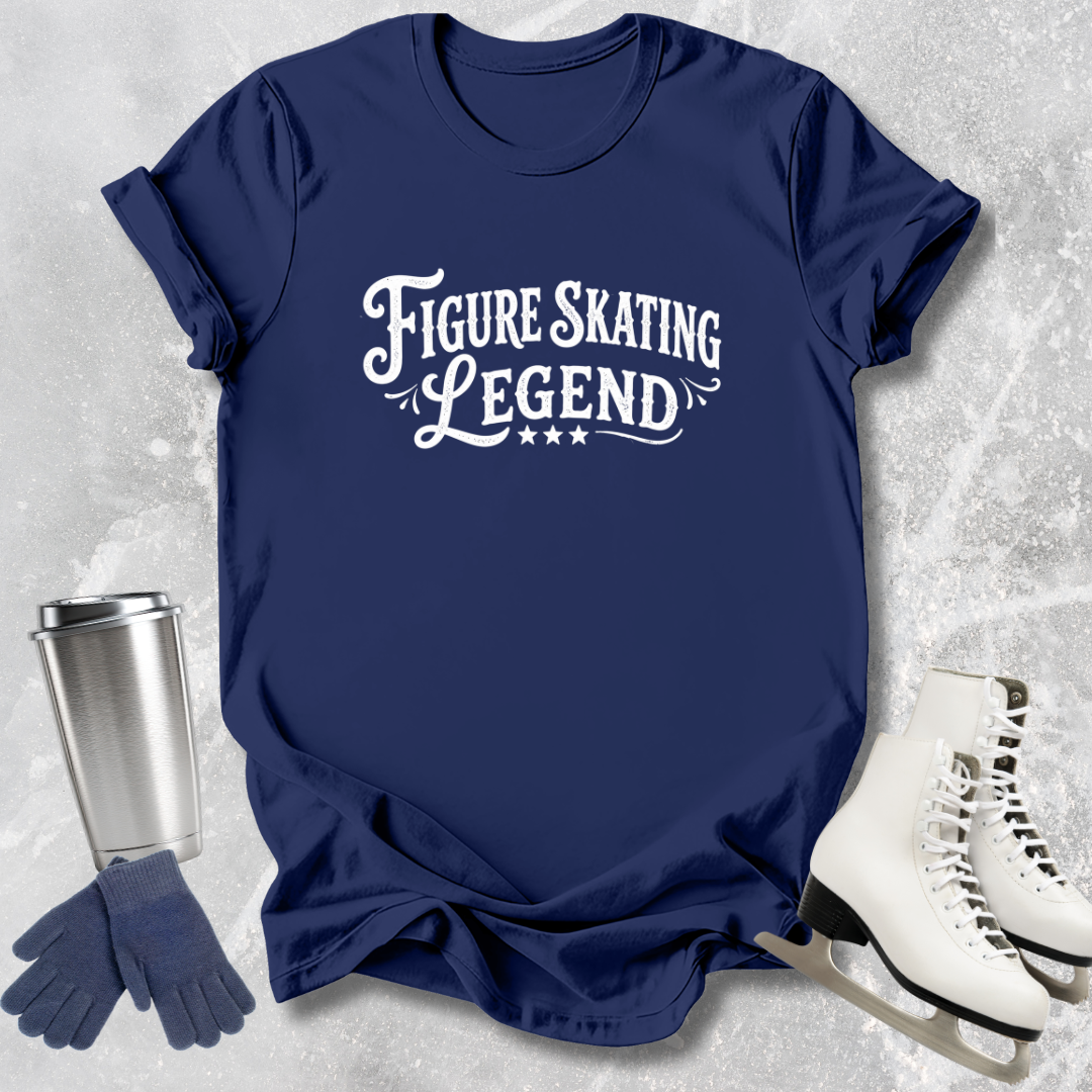 Navy blue t-shirt with 'Figure Skating Legend' text, next to ice skates and a tumbler on a textured gray background.