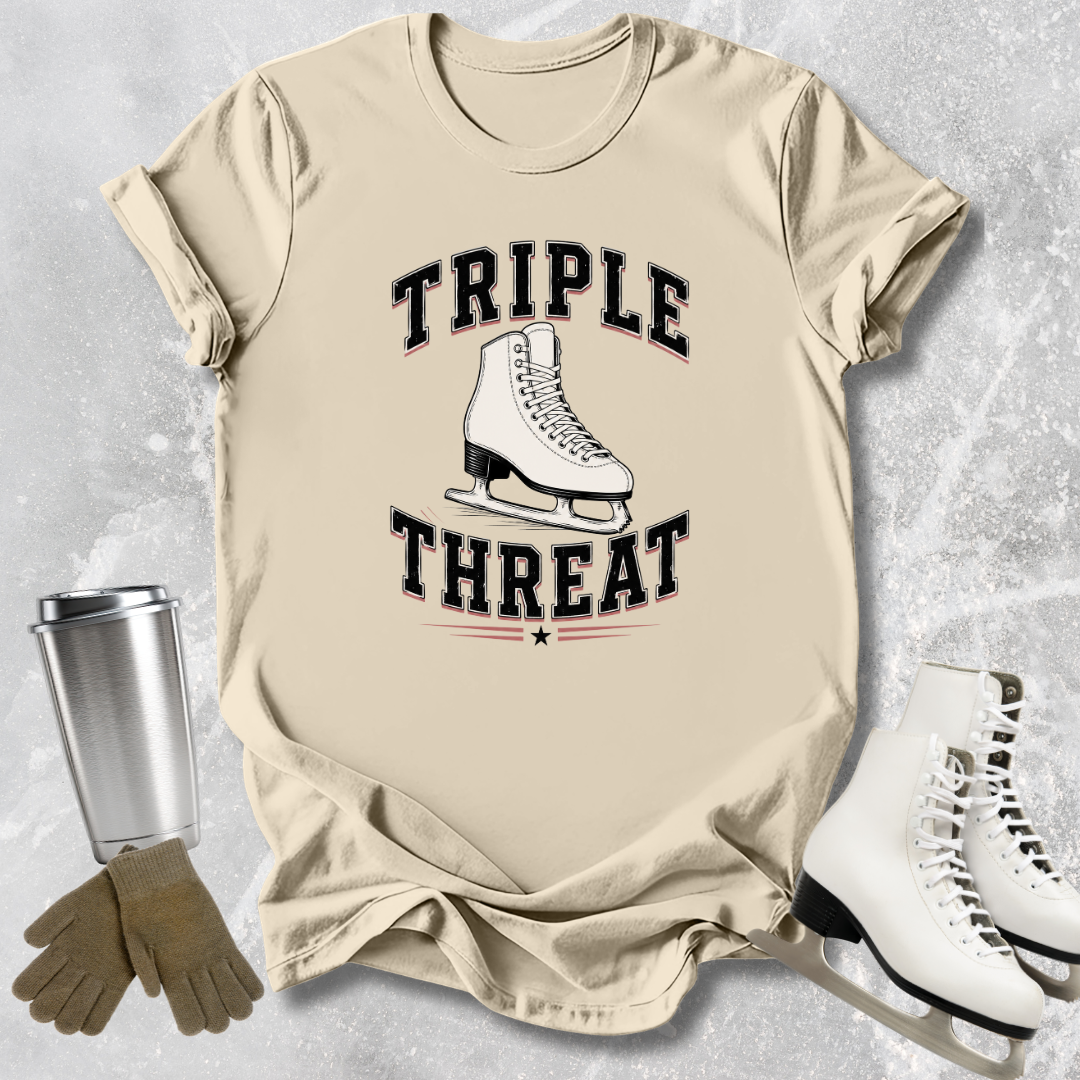 Beige t-shirt with 'Triple Threat' graphic and ice skate design, placed on a textured surface with ice skates and a tumbler.